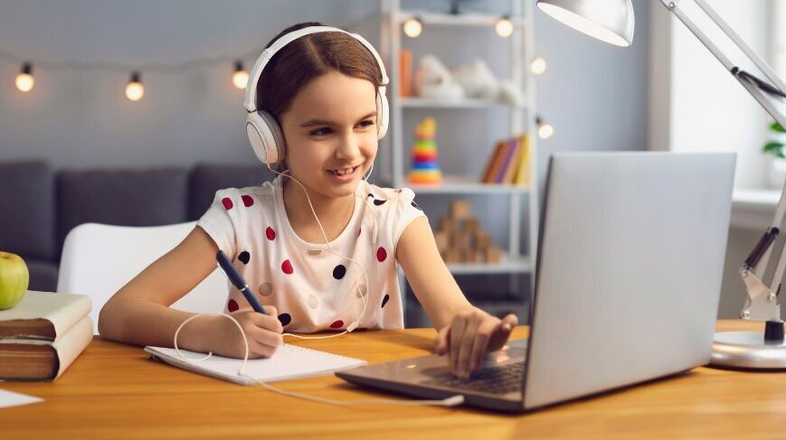 A middle-school student wearing headphones smiles and participates in an online class on her laptop, illustrating how EDUPRIZE Online keeps students engaged, connected, and able to learn from anywhere.