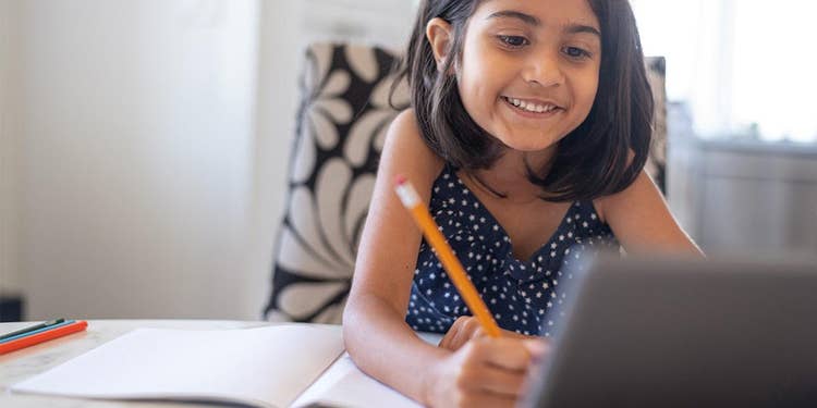 A student attends a live online class at home, engaged in virtual learning with a headset and laptop through EDUPRIZE Online.