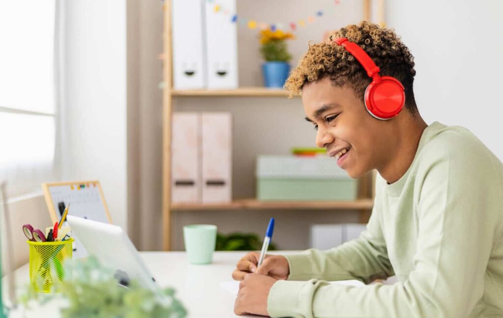 A high school student in Arizona attends a live online class at home, participating with a headset while viewing the teacher on screen through EDUPRIZE Online.